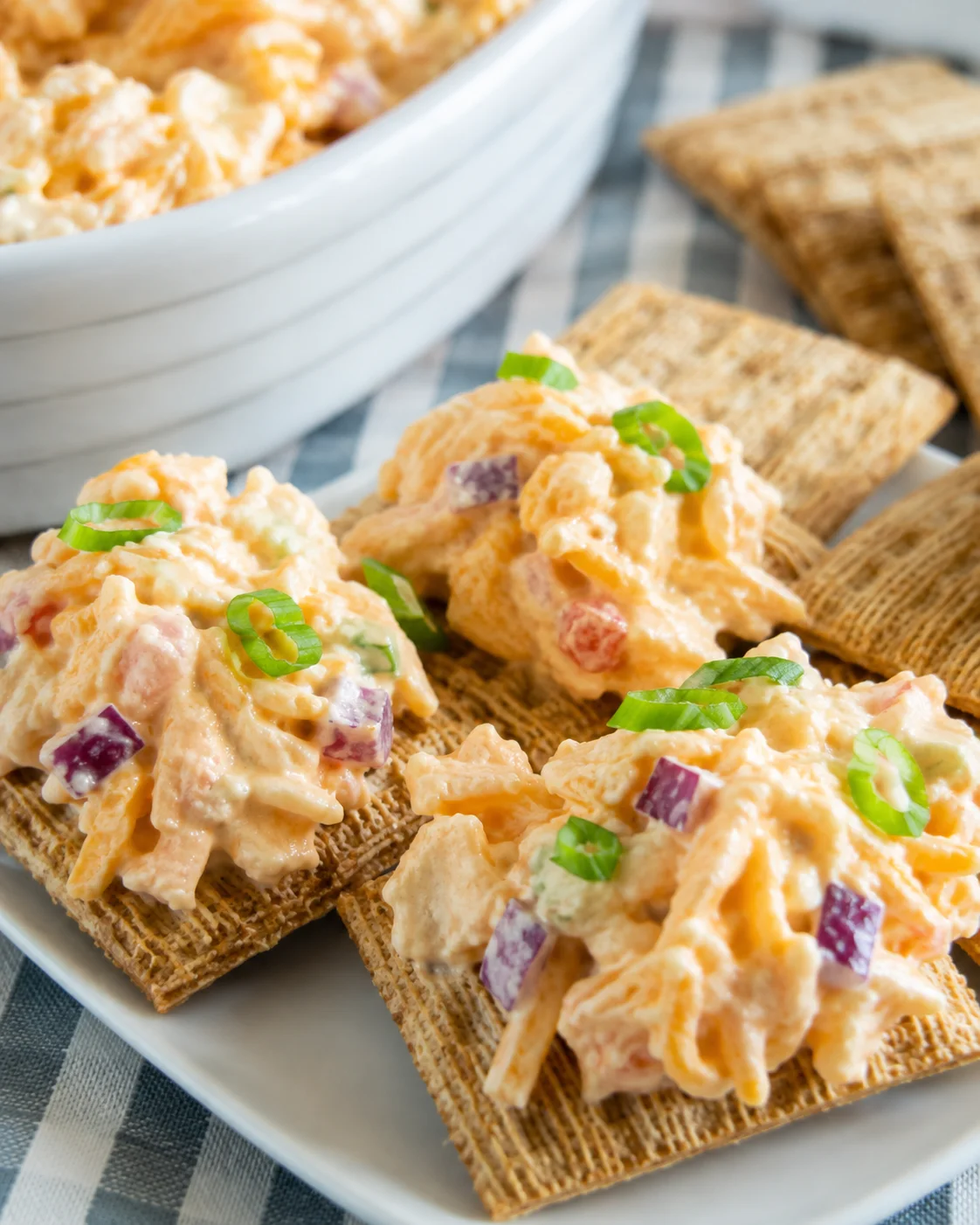 Spoonfuls of 5 minute crack dip piled on crackers with a bowl of dip in background