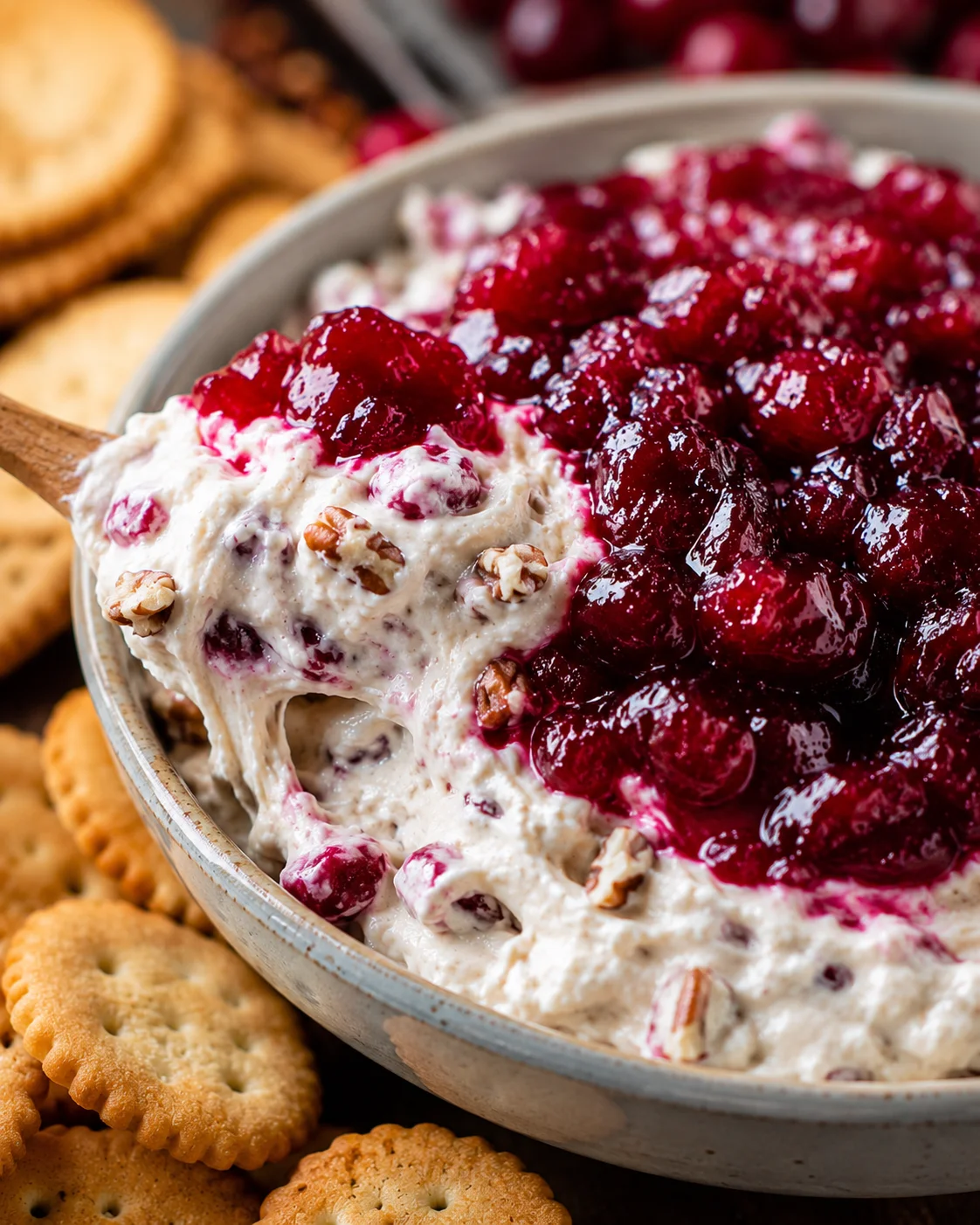 Bowl of cranberry cream cheese dip topped with glossy cranberry sauce and pecans next to crackers