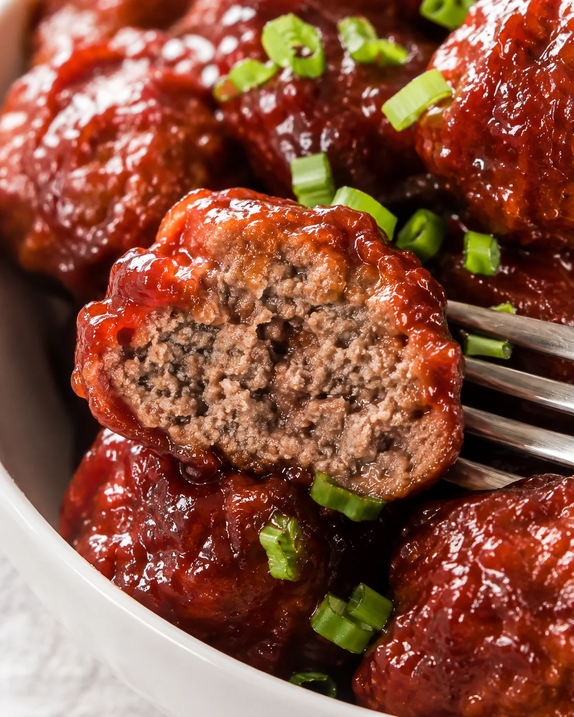 Fork holding a halved cranbery meatball showing the cooked interior and sauce