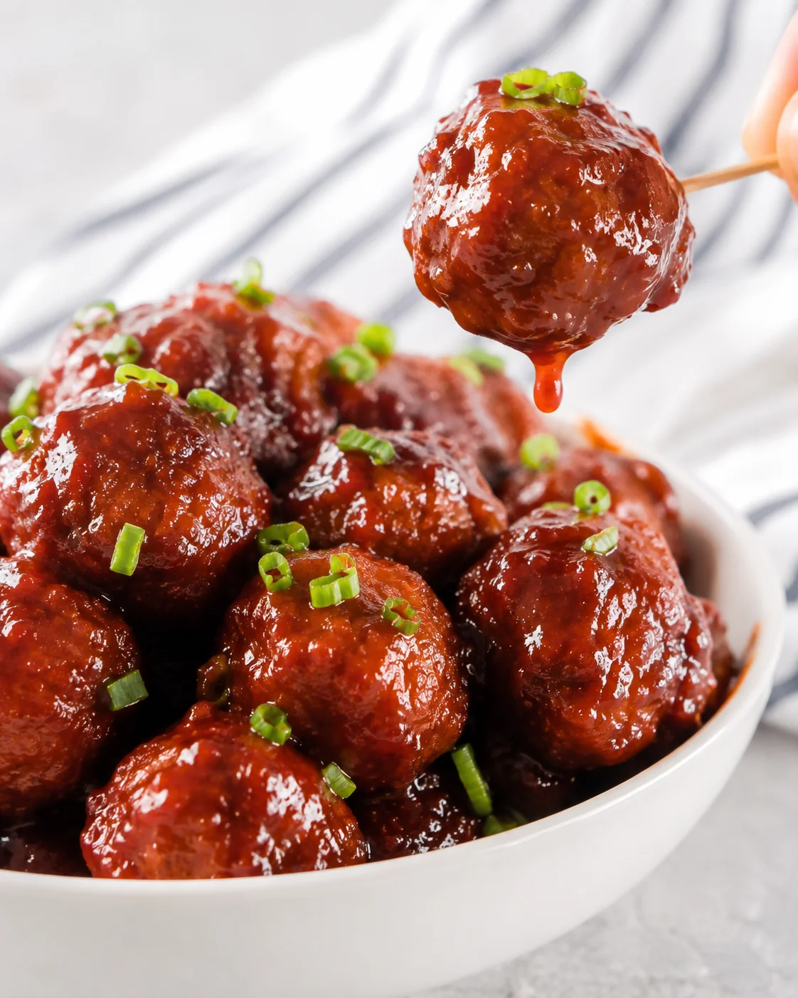 Single cranberry-glazed meatball on a toothpick dripping sauce above a bowl
