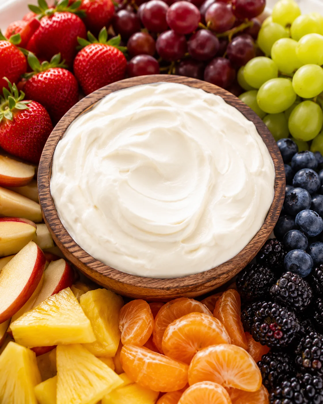 Bowl of cream cheese fruit dip surrounded by assorted fresh fruit