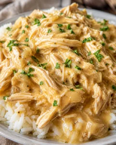 Close-up of shredded crockpot chicken coated in creamy gravy over rice with chopped parsley