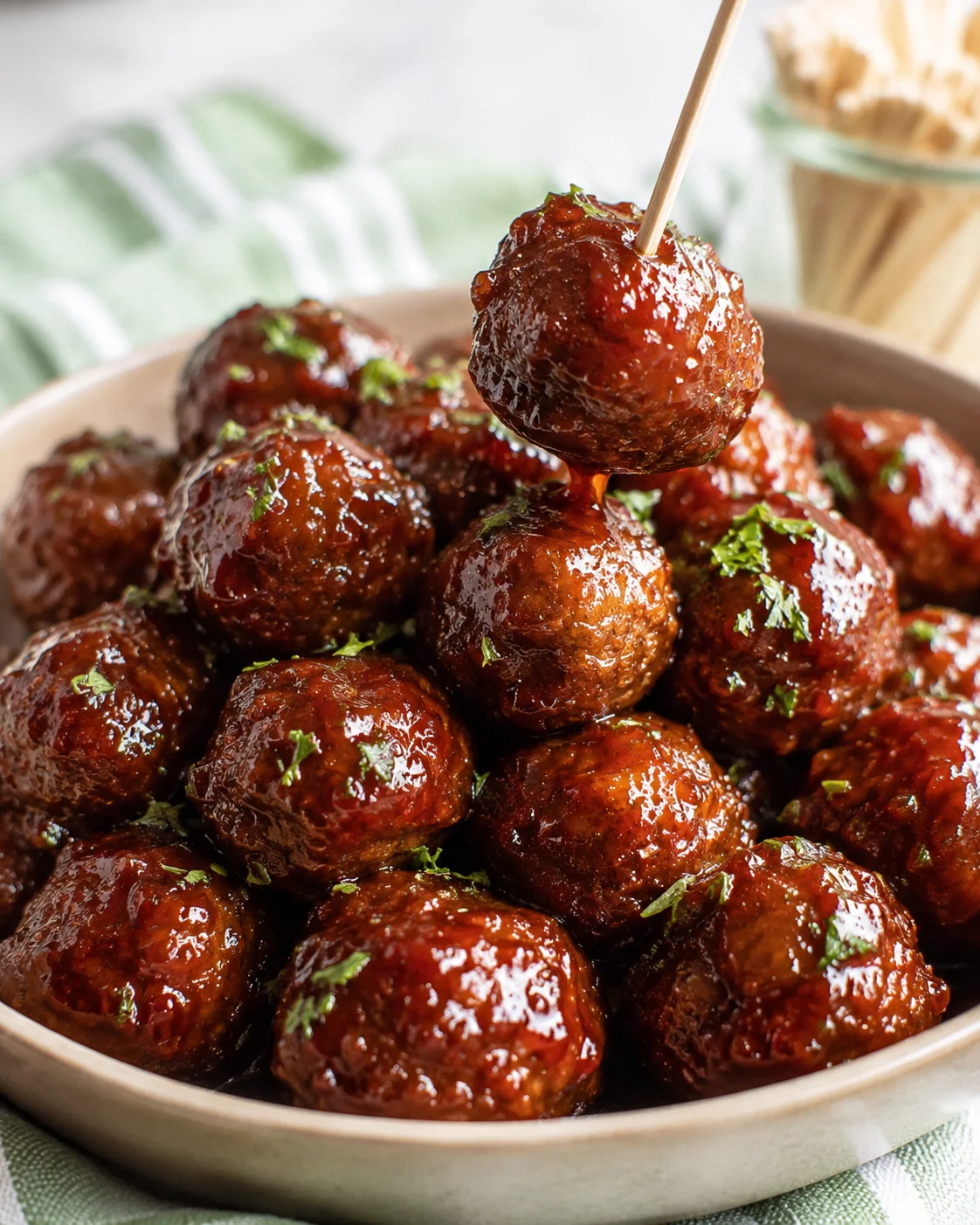 Single crockpot meatball lifted on a skewer with grape jelly sauce dripping