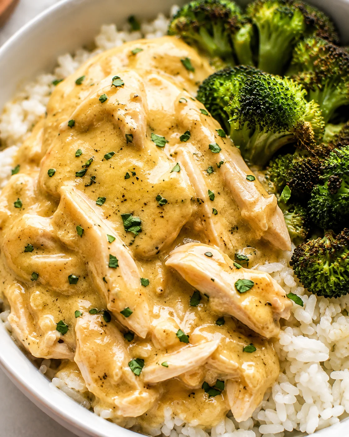 Crockpot ranch chicken served over white rice with roasted broccoli in a bowl