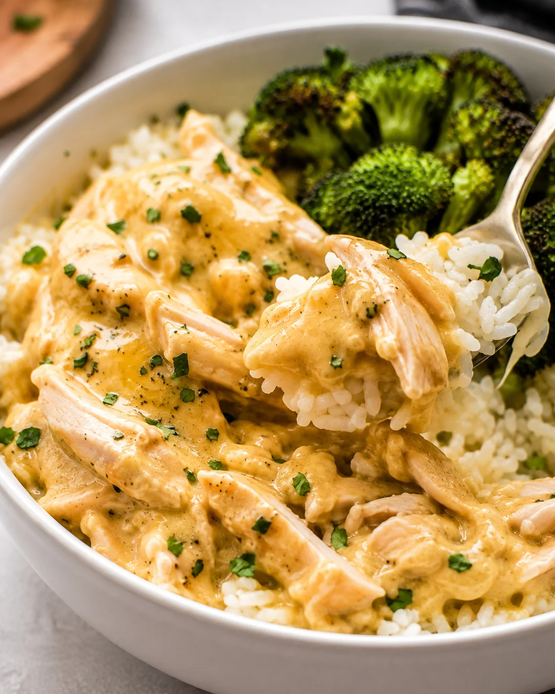Spoon lifting a bite of crockpot ranch chicken and rice from a bowl with broccoli