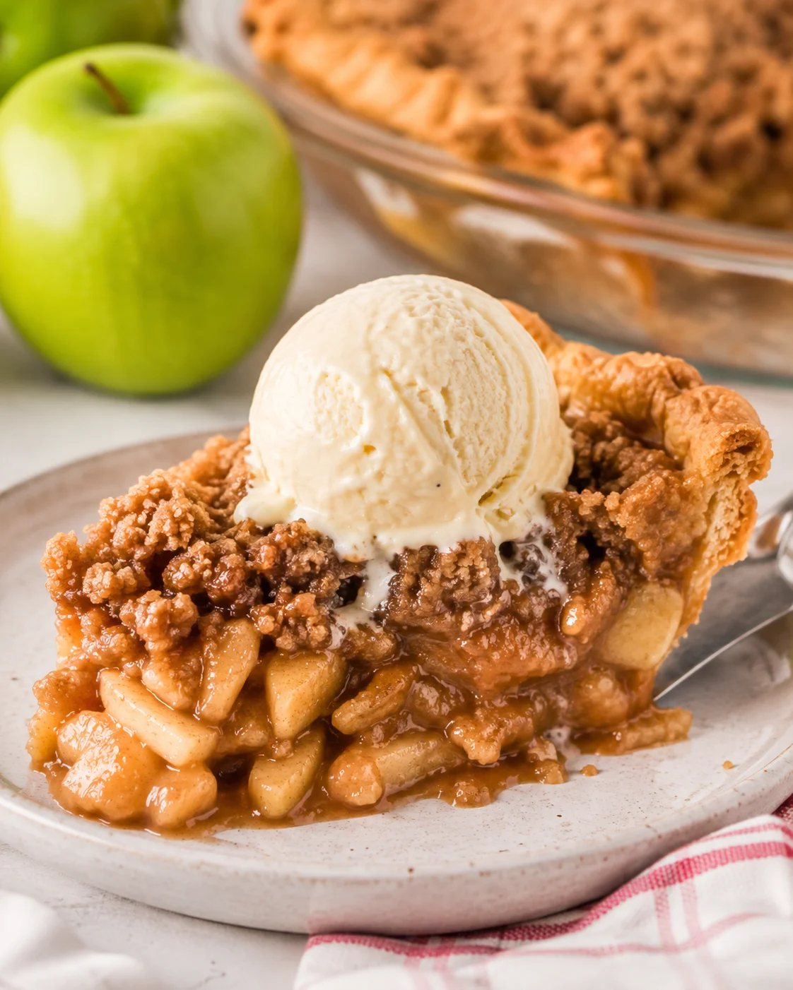 Side view of a slice of Dutch apple pie with crumb topping and a scoop of vanilla ice cream