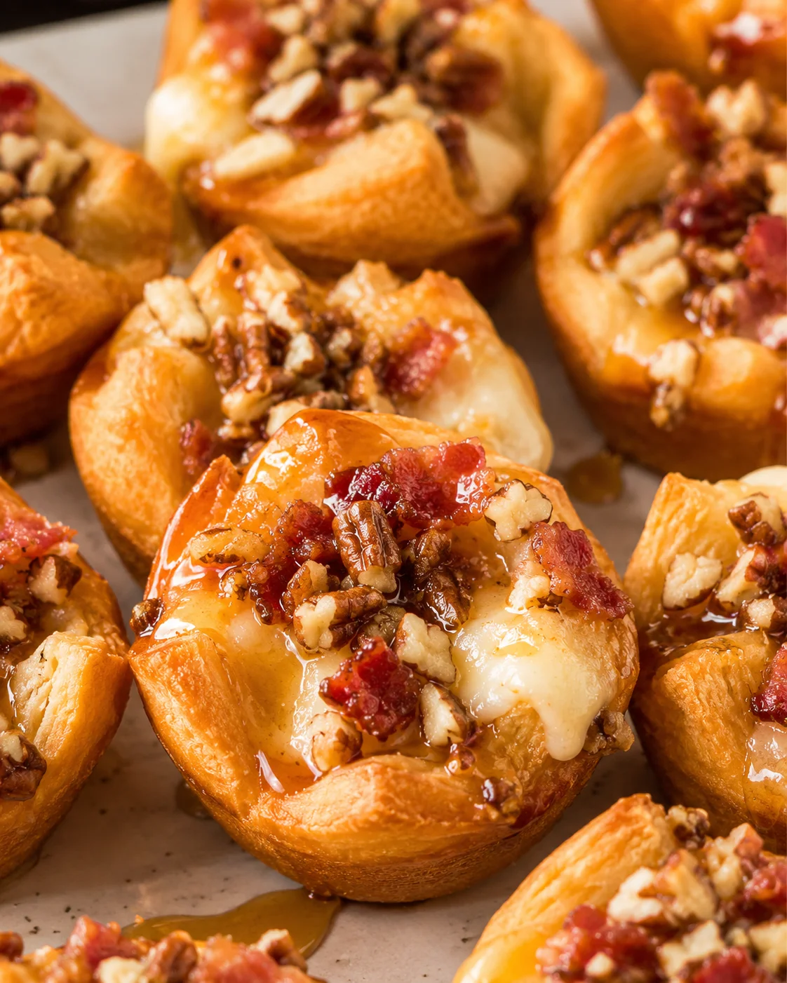 Close-up of baked Easy Bacon Brie Bites with melted brie, chopped pecans, bacon and maple glaze