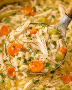 Close-up of a ladleful of chicken and rice soup showing rice grains, shredded chicken, carrot slices, and broth