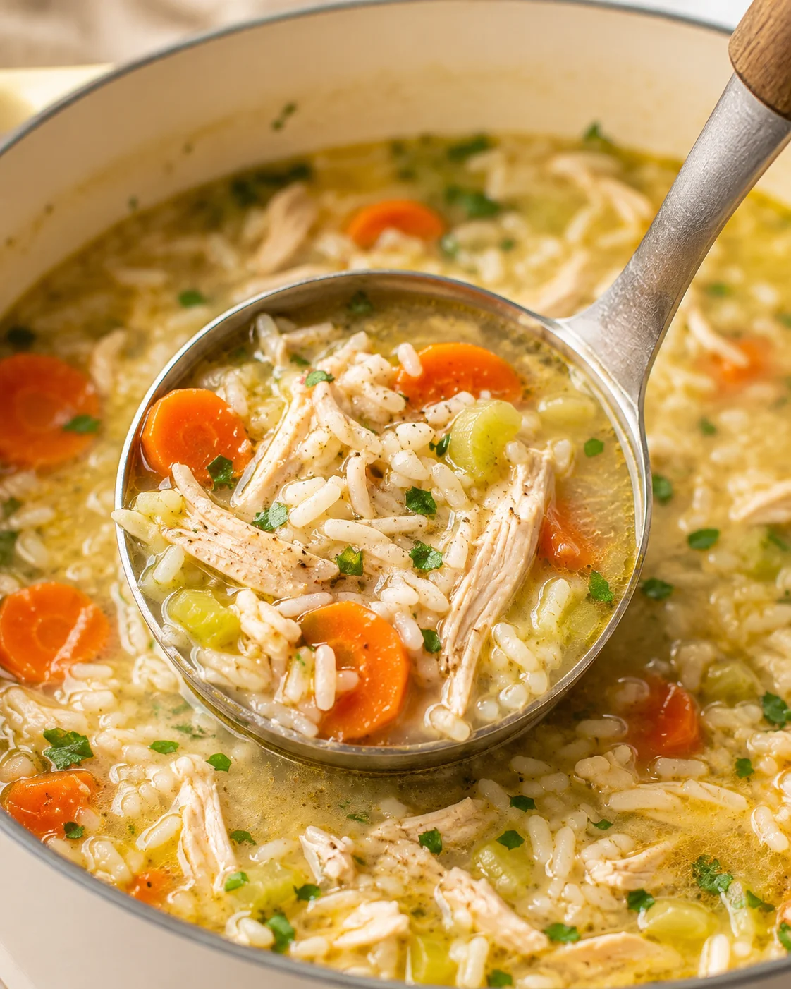 Ladle scooping chicken and rice soup from a pot showing shredded chicken, rice, carrots, and parsley