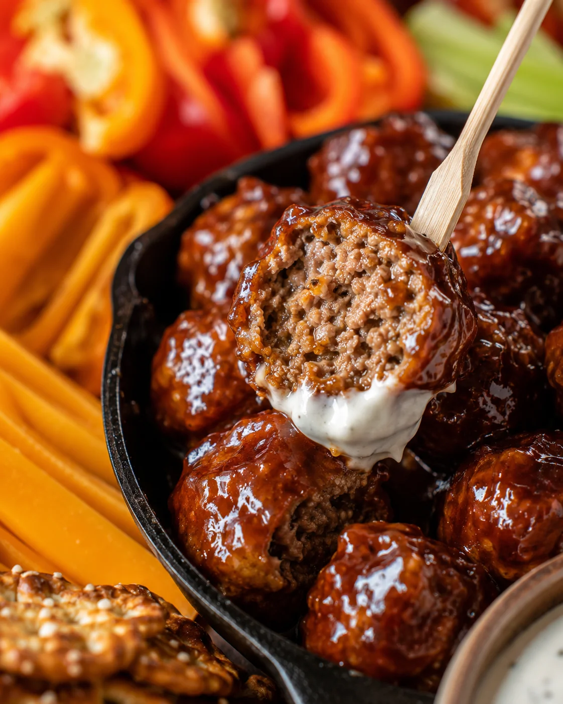 Close-up of a sauced meatball pierced on a pick showing the cooked interior and ranch dip