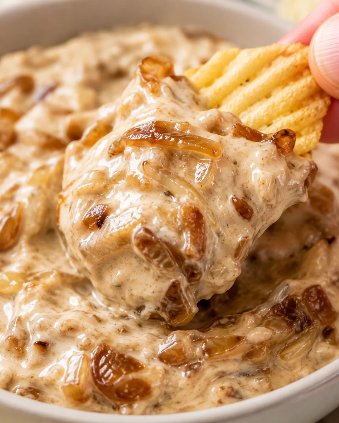 Close-up detail of caramelized onion dip clinging to a chip showing glossy onions and creamy base