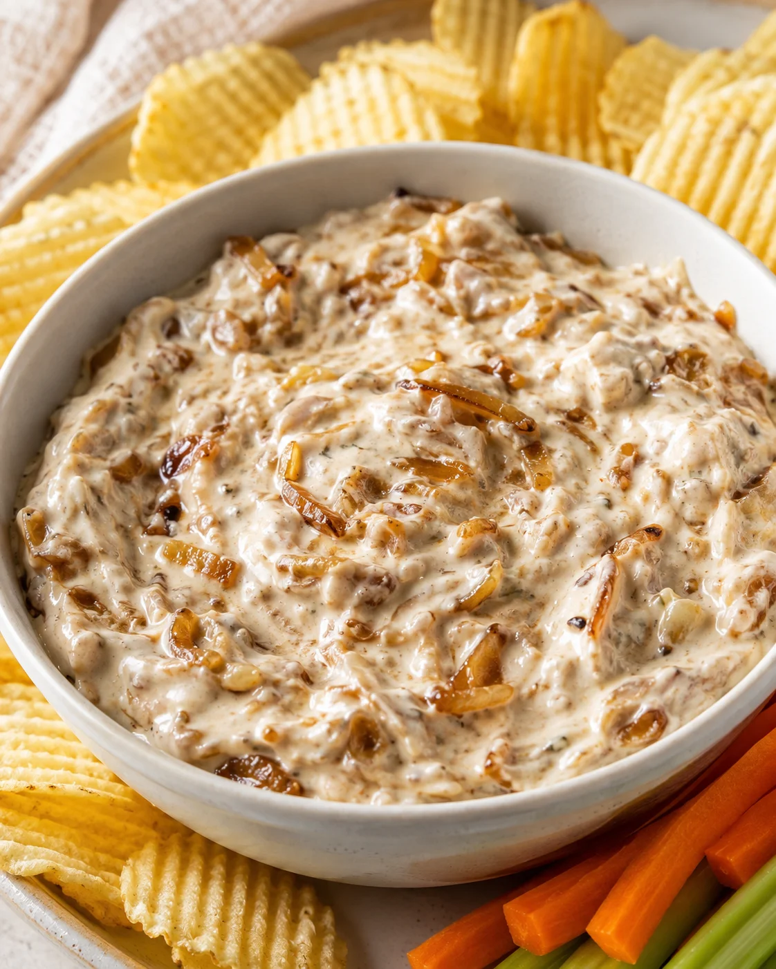 Bowl of Ina Garten-style caramelized onion dip served with potato chips and vegetable sticks
