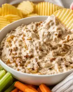 Ridged potato chip scooping a spoonful of caramelized onion dip from a bowl
