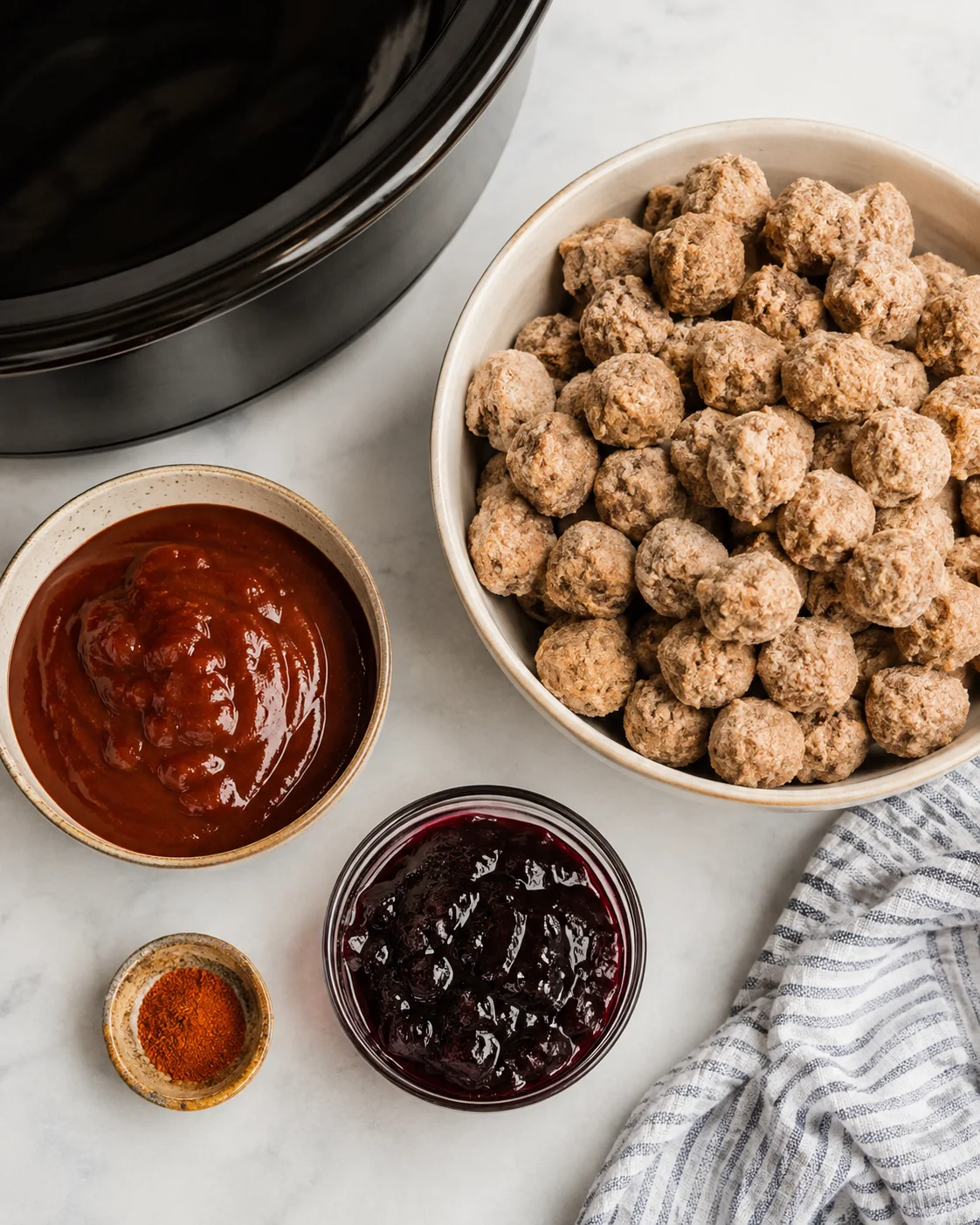 Top-down view of frozen meatballs, barbecue sauce, grape jelly and a spice beside a slow cooker