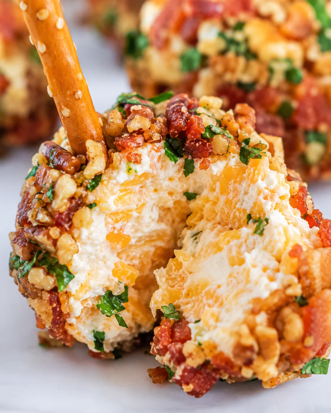 Close-up of a split mini cheese ball showing creamy cheese and shredded cheddar inside, coated in bacon and nuts