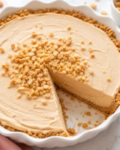 Whole no-bake peanut butter pie in a white fluted dish with chopped peanuts on top and one slice removed