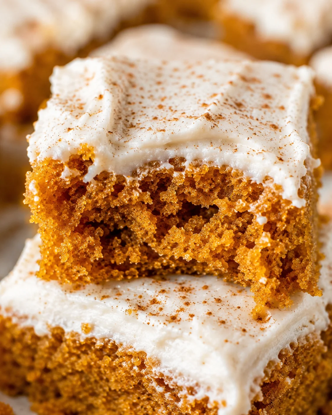 Close-up of moist pumpkin bars topped with creamy frosting and a light dusting of spices.