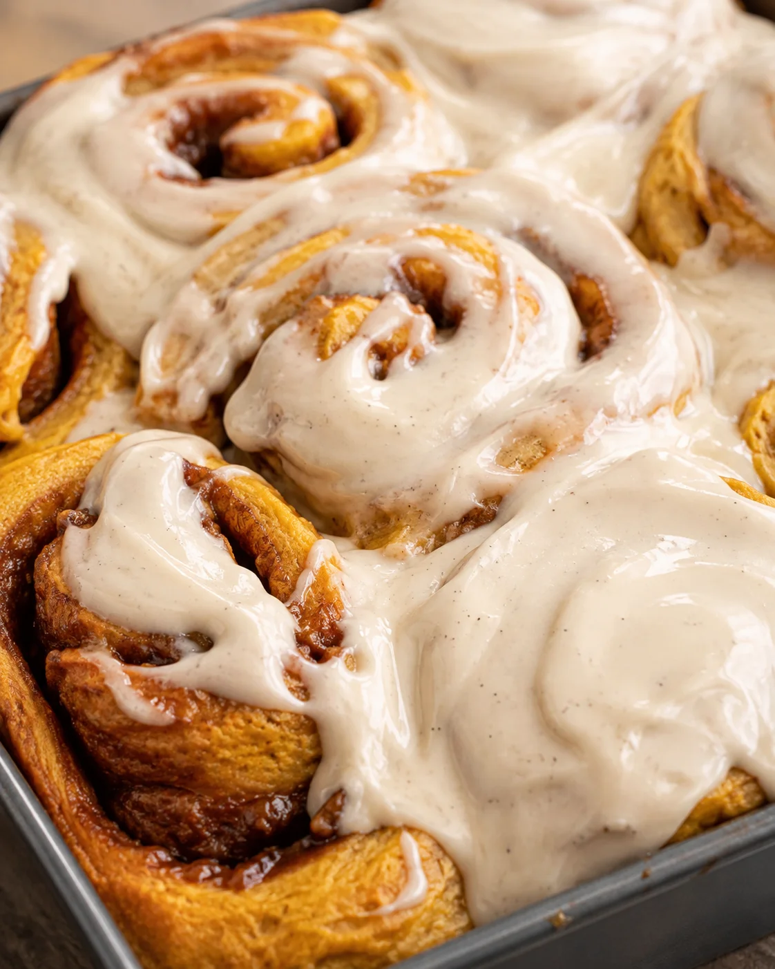 Close-up of soft pumpkin cinnamon rolls topped with creamy vanilla bean maple frosting.