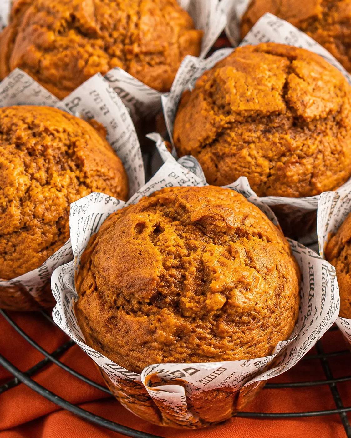 Fresh bakery-style pumpkin muffins placed in paper liners on a cooling rack.