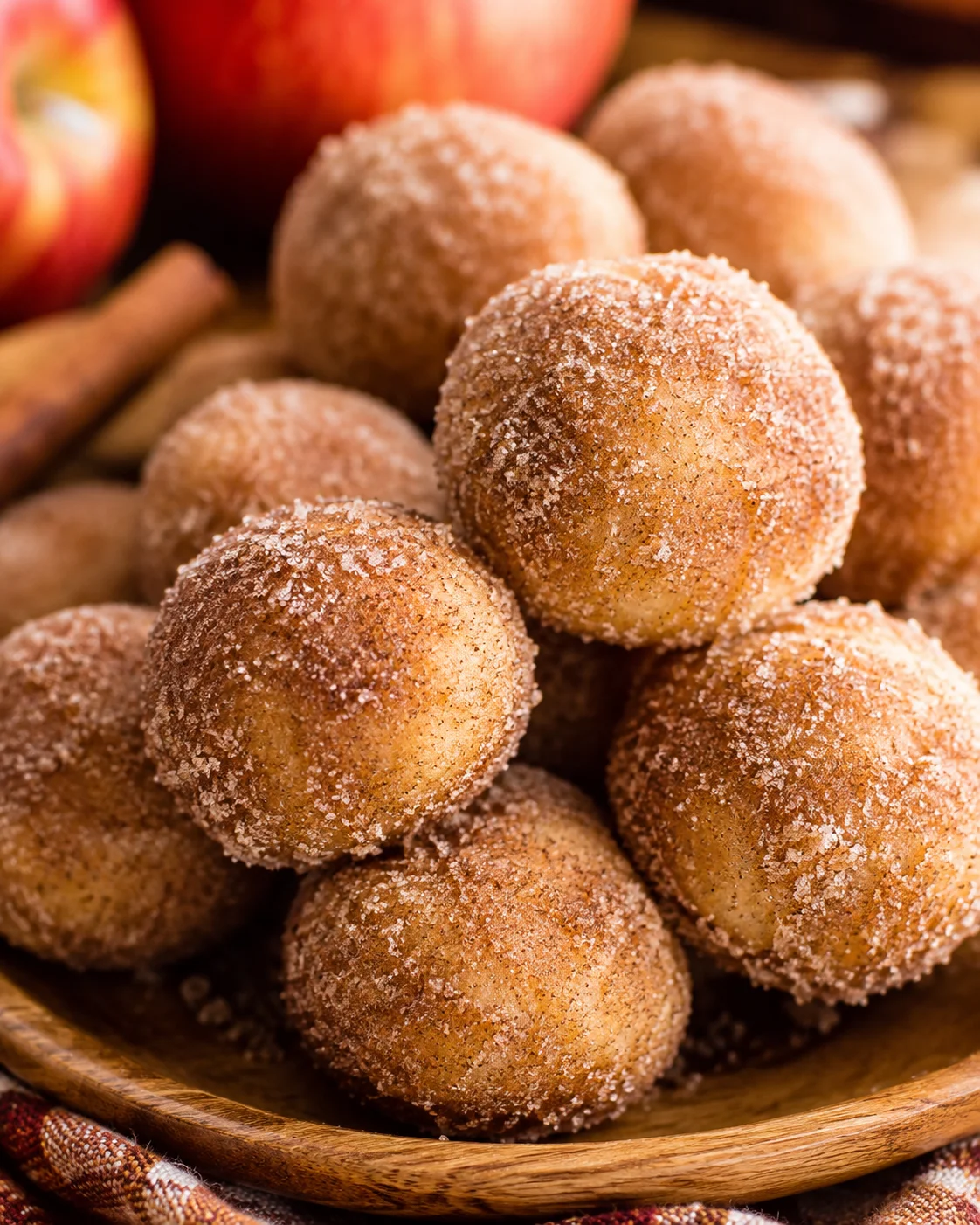 Close-up of cinnamon-sugar coated baked apple cider donuts on a wooden plate with apples in background.