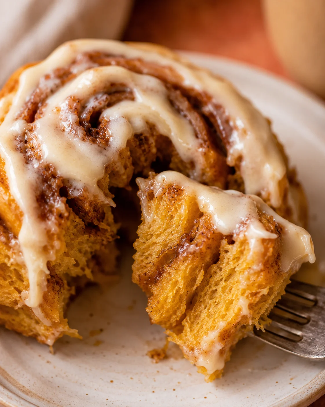 Close-up of freshly baked pumpkin cinnamon rolls with creamy frosting, on a white plate