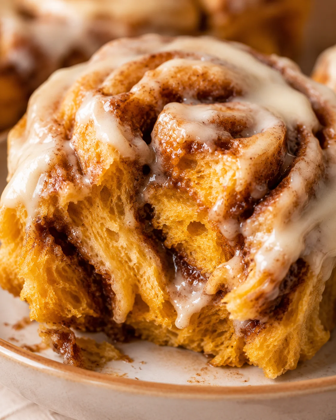Close-up of warm, fluffy pumpkin cinnamon rolls topped with creamy frosting