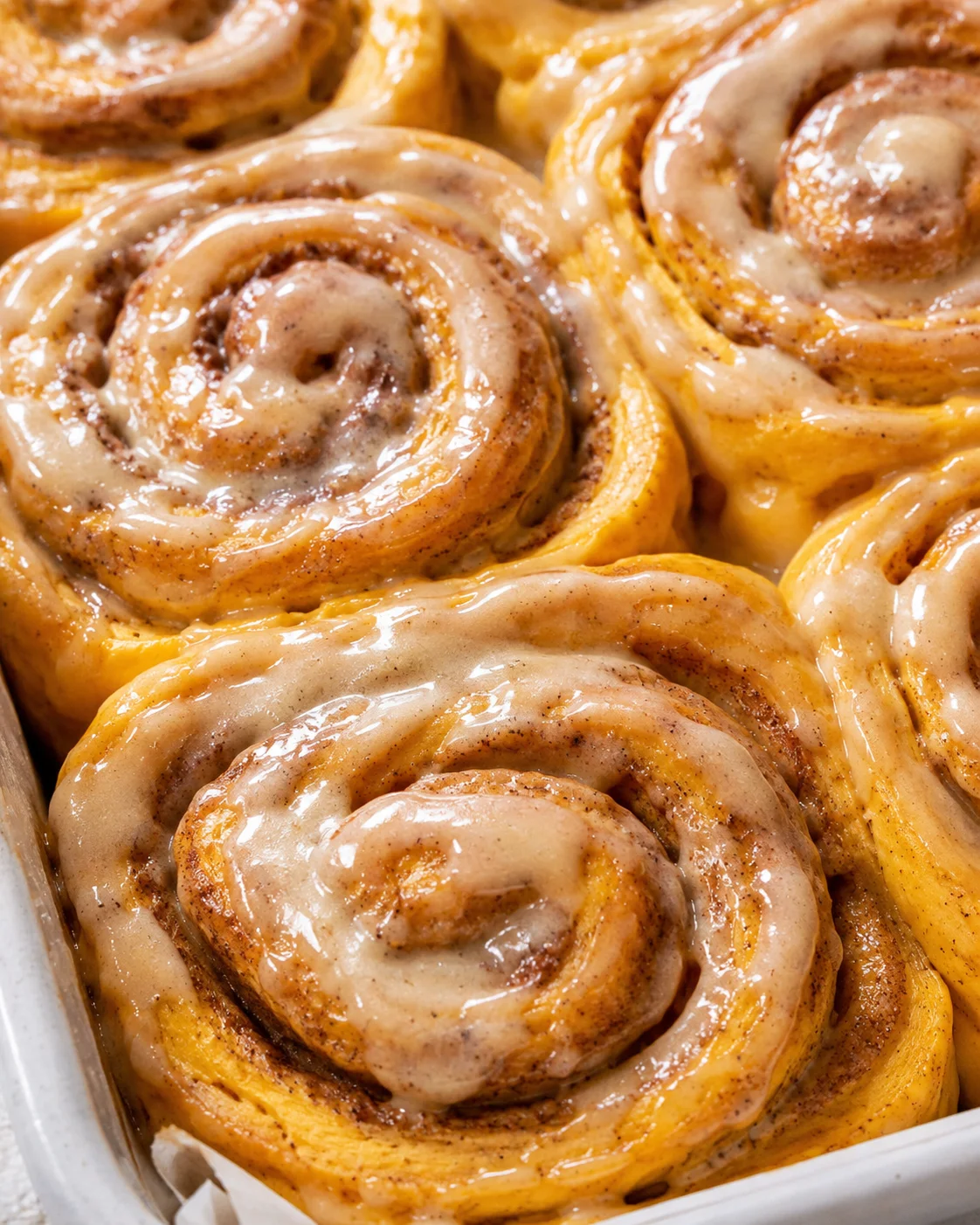 Close-up of soft pumpkin cinnamon rolls topped with coffee maple frosting.
