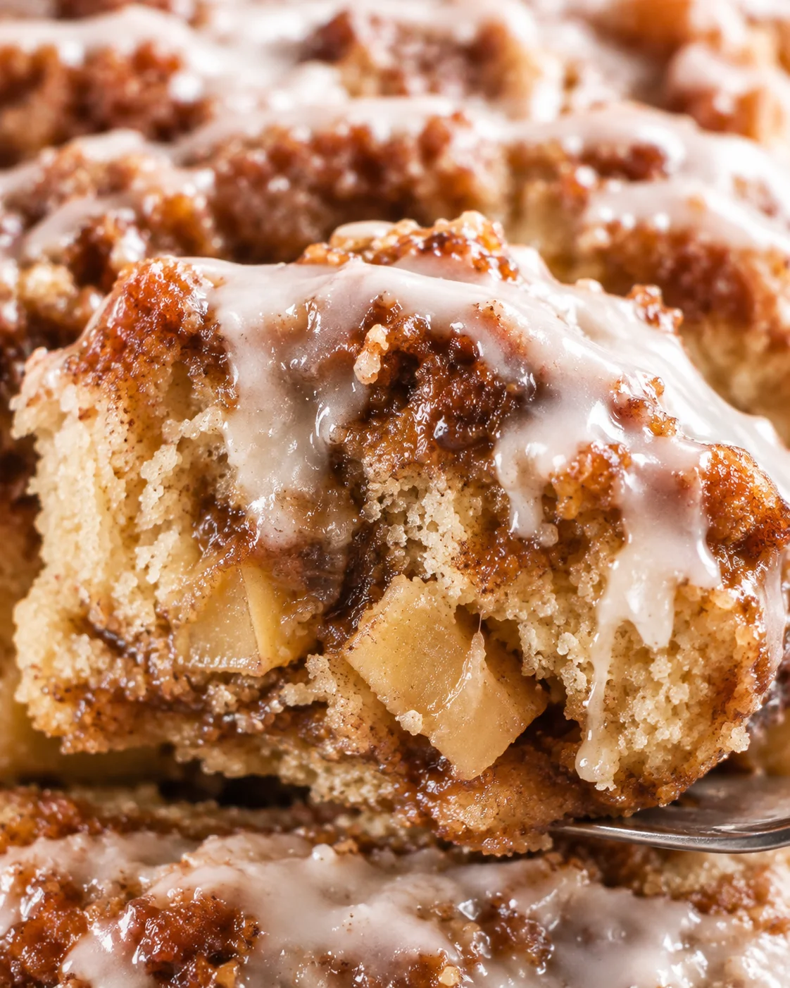 Close-up of a moist apple fritter bread loaf topped with glaze, filled with apples and cinnamon.
