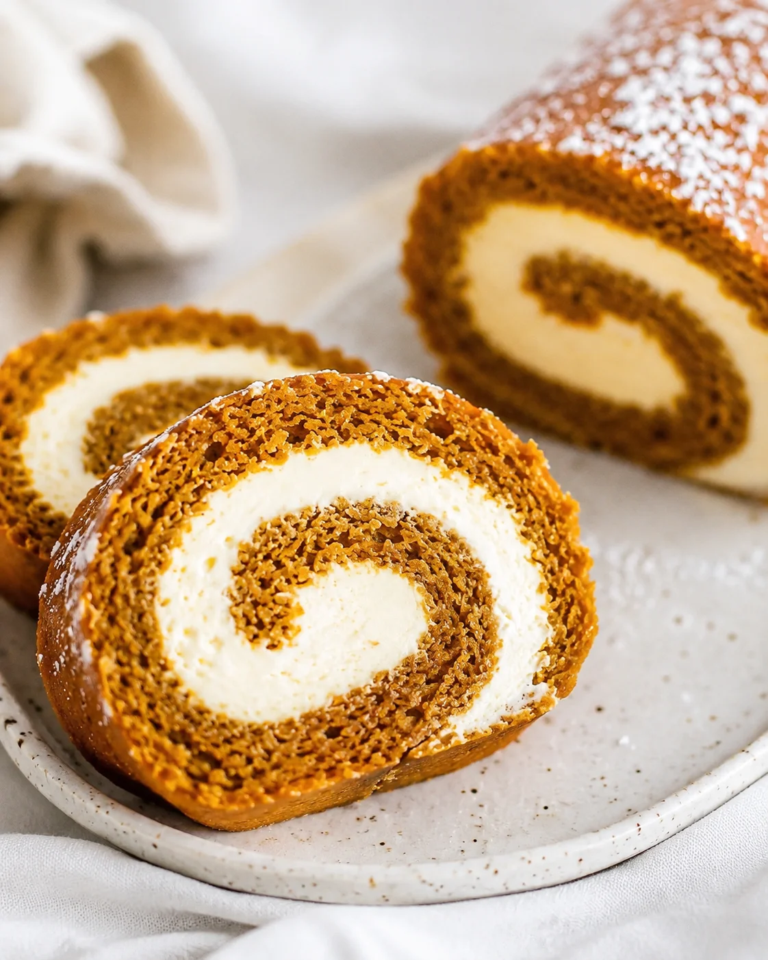 Close-up of a sliced pumpkin roll with cream cheese filling on a white plate.