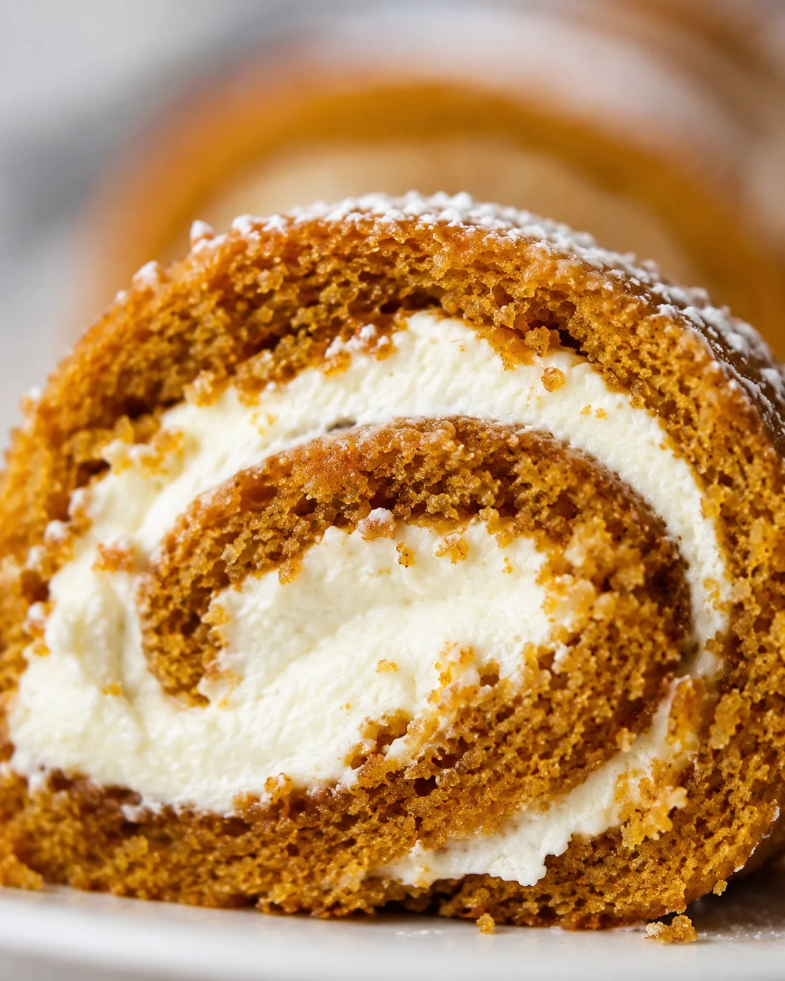 A close-up of a sliced pumpkin roll with cream cheese filling, dusted with powdered sugar.