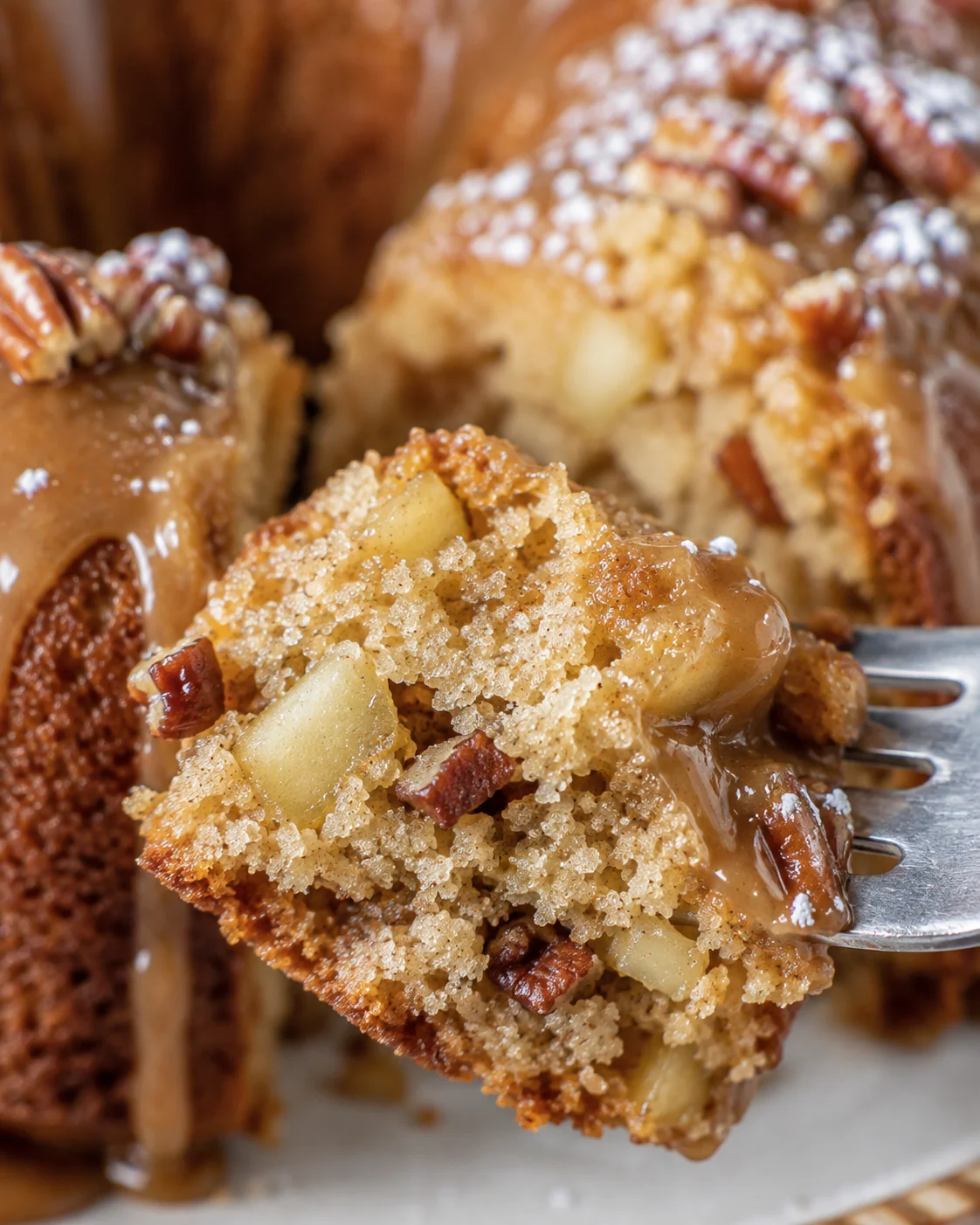 Close-up of a slice of moist, apple-filled gluten-free cake with pecans and glaze