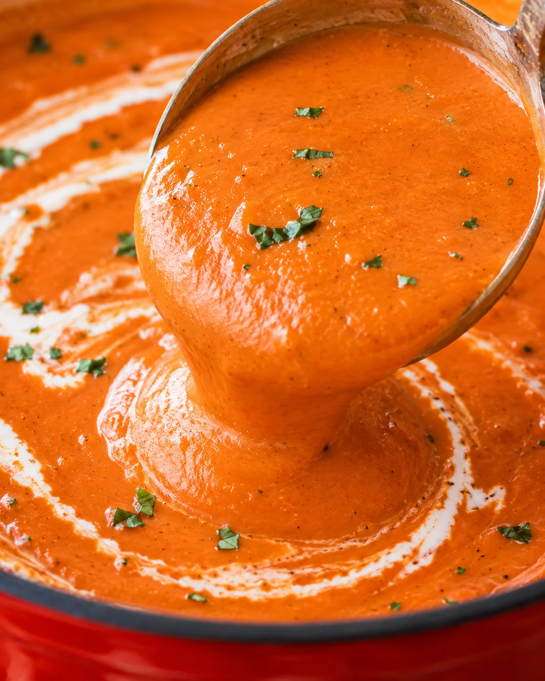 Smooth, rich tomato bisque being poured from a pot with garnished herbs on top.