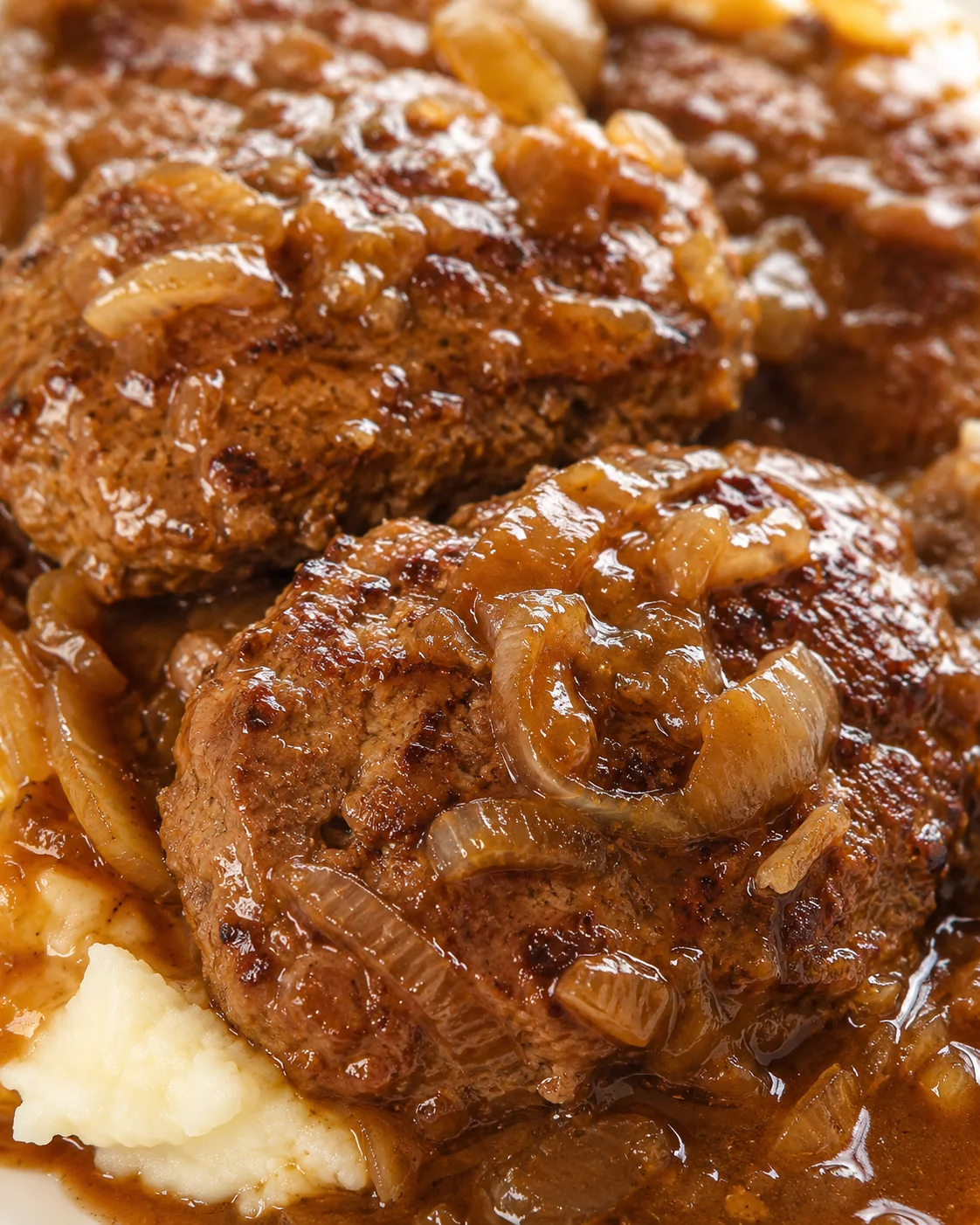 Close-up of Salisbury steak patties smothered in rich onion gravy, served over mashed potatoes