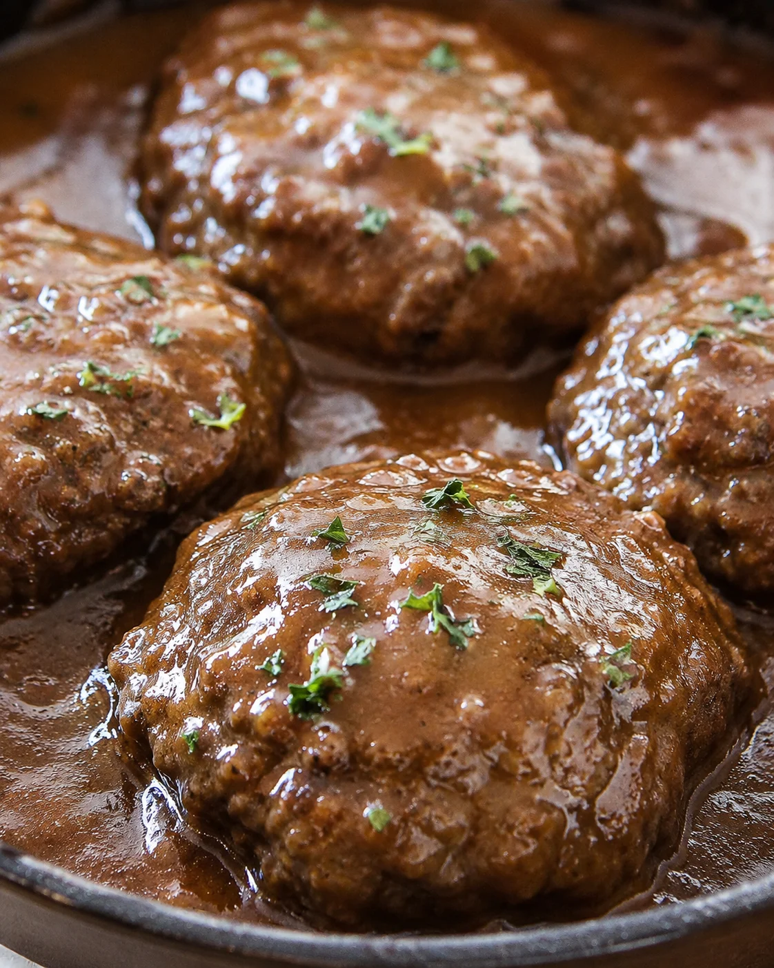 Close-up of Salisbury steak patties covered in gravy with fresh herbs