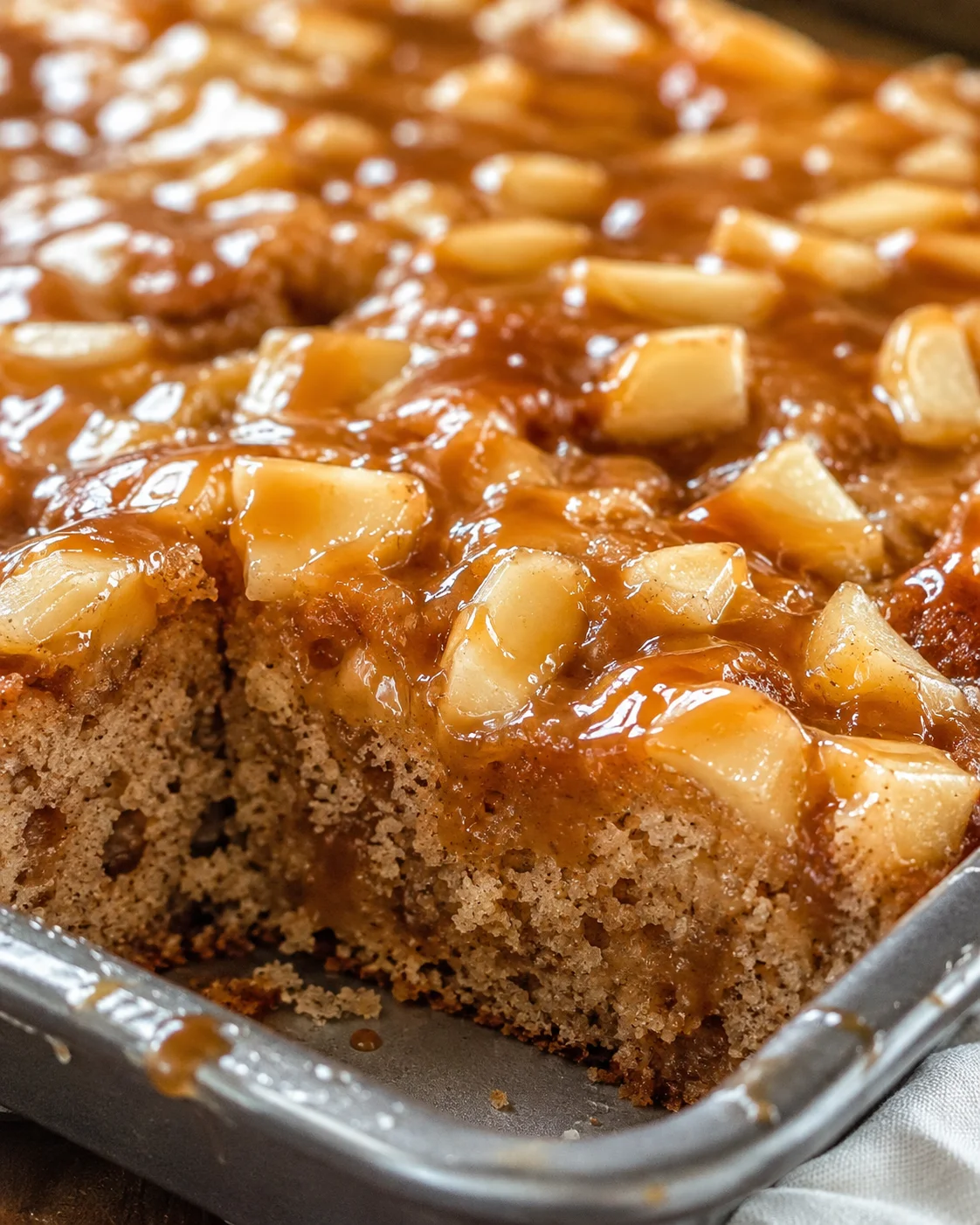 Moist apple cake topped with caramel glaze in a large baking sheet.