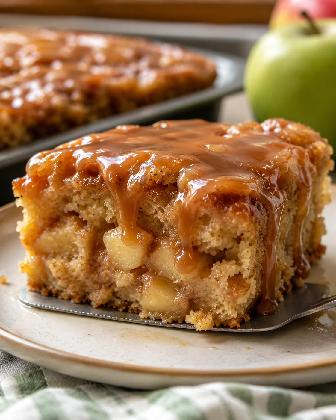 Moist cinnamon apple cake topped with caramel glaze on a serving plate.