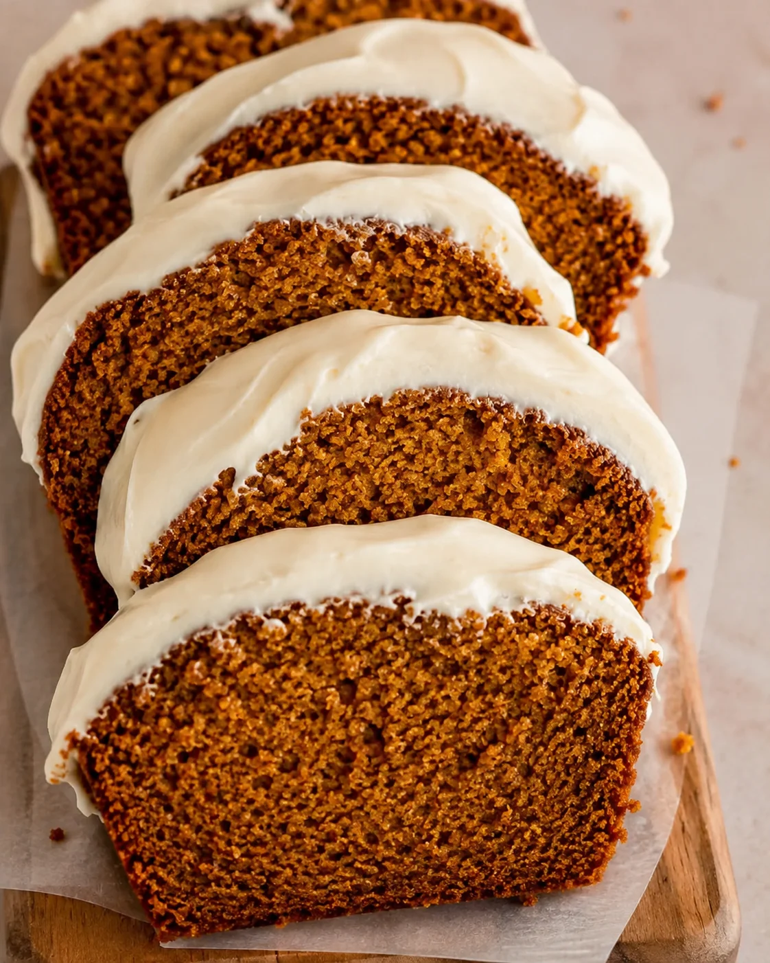 Sliced pumpkin bread with creamy white frosting on top, arranged on a wooden board