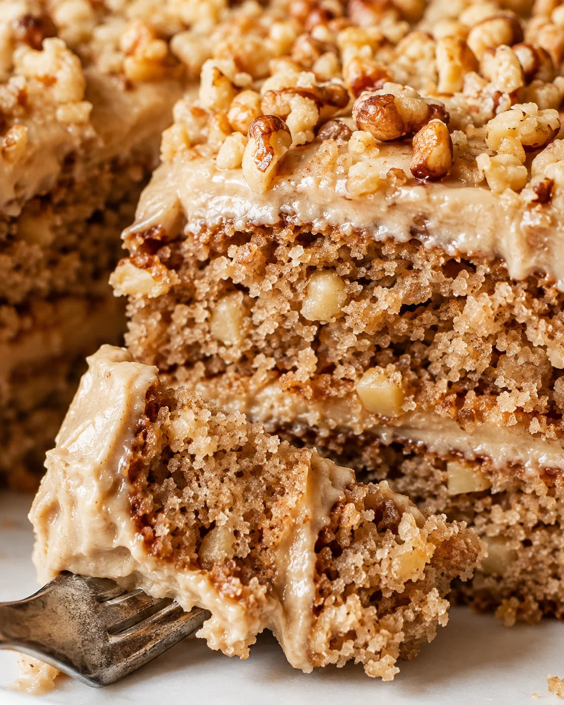 Close-up of moist apple spice cake topped with chopped walnuts and cream frosting.