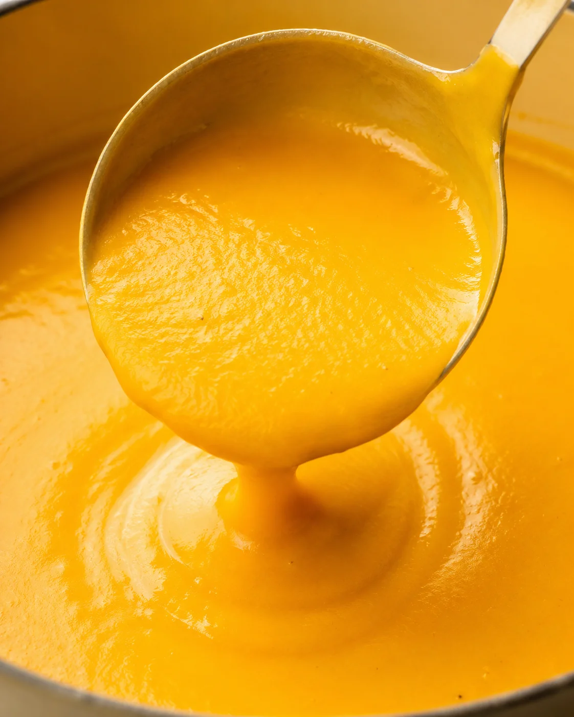 Close-up of a shiny ladle scooping bright orange cheese sauce from a pot