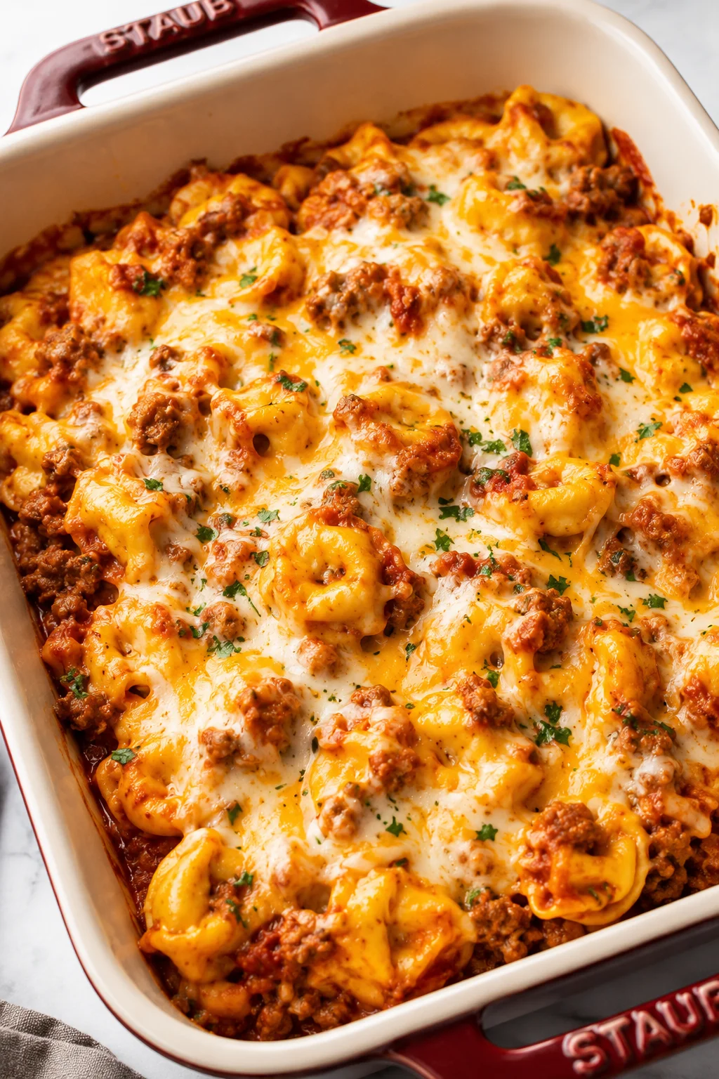 baked pasta casserole topped with melted cheese in a red Staub dish
