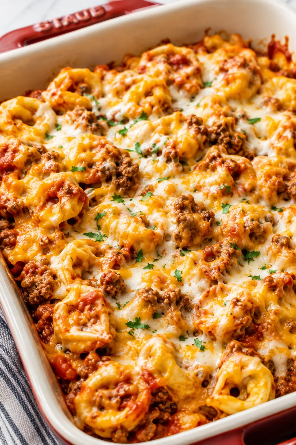 Cheesy baked pasta with meat sauce in a red Staub dish.
