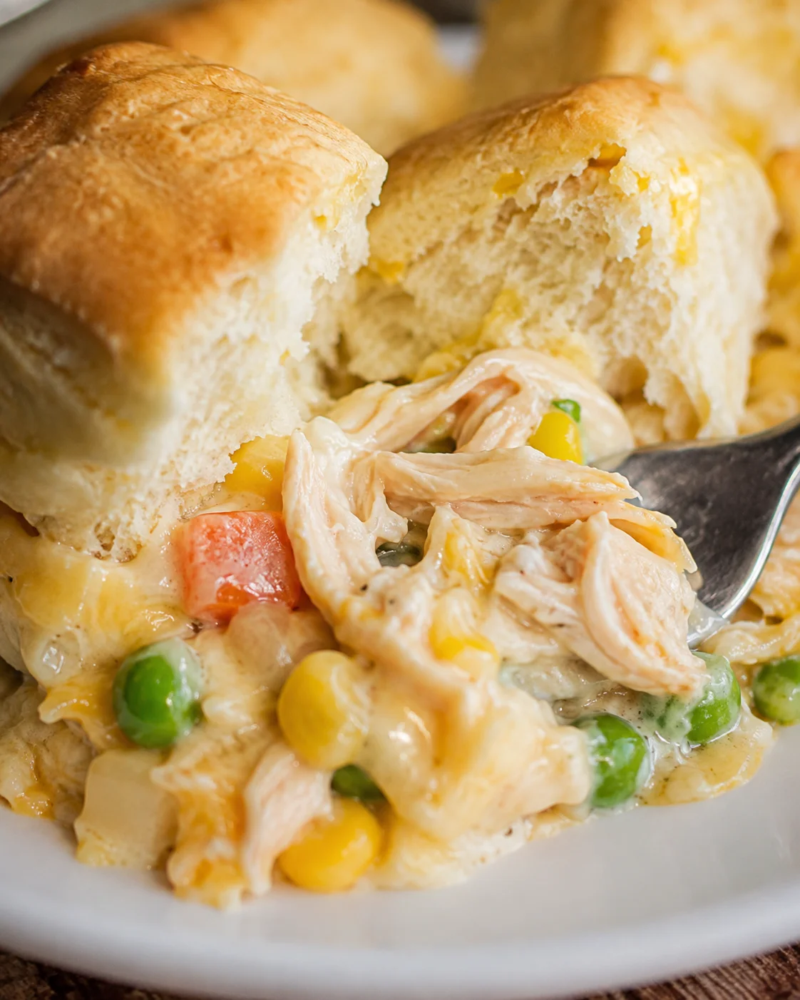 A close-up of a homemade chicken pot pie topped with flaky biscuits, filled with vegetables and chicken.