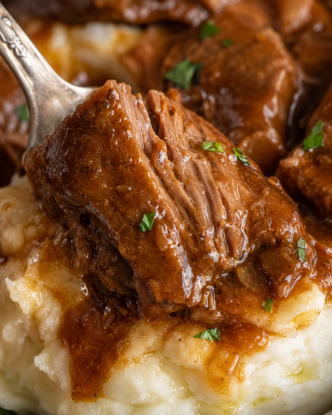 Close detail of a fork pulling apart a tender piece of slow cooker beef tips over mashed potatoes
