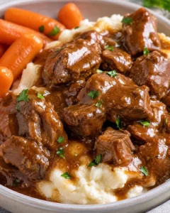 Close-up of slow cooker beef tips in rich gravy served on mashed potatoes with carrots