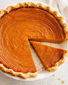 Overhead view of a sweet potato pie with one slice removed showing the smooth orange filling and fluted crust