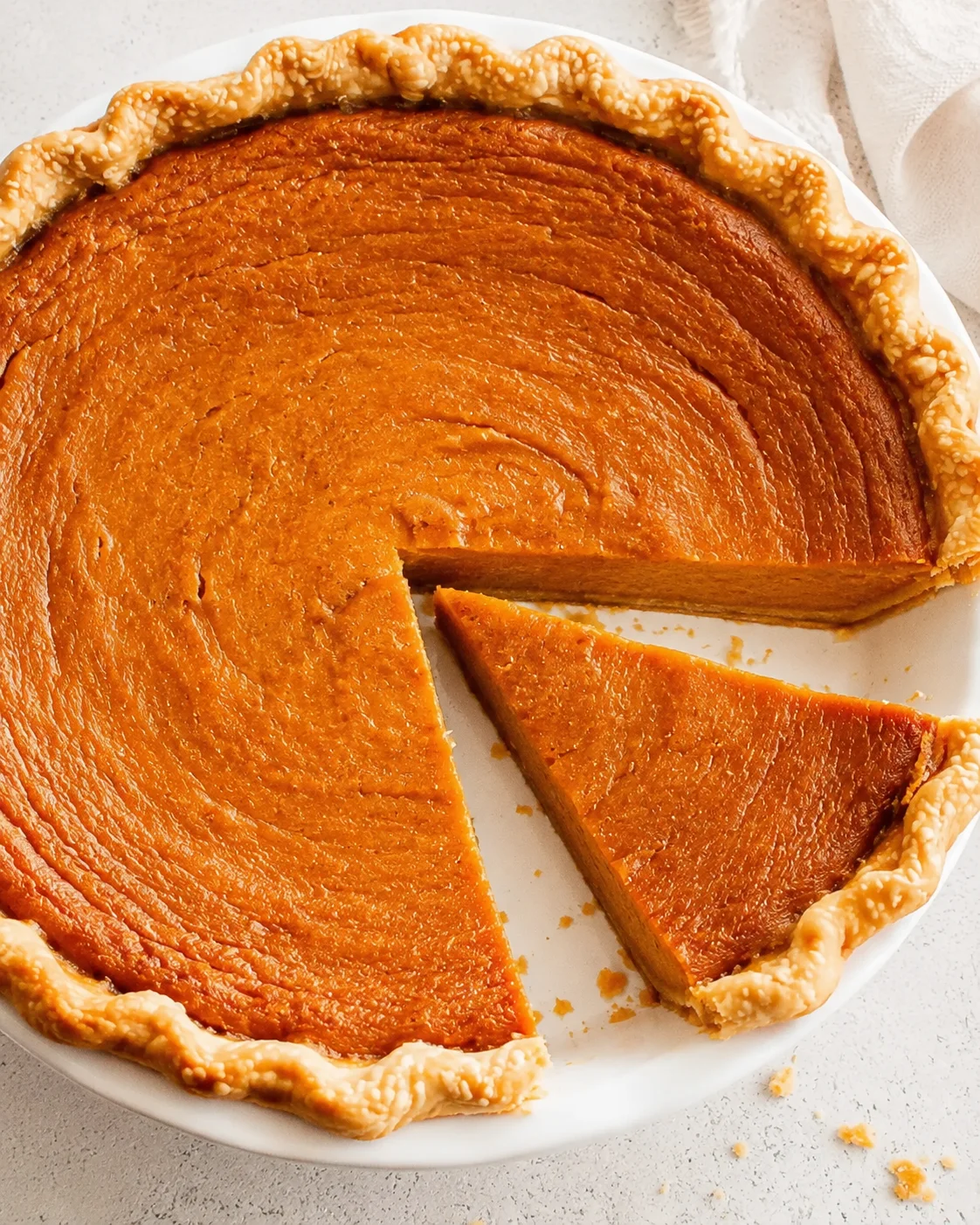 Overhead view of a sweet potato pie with one slice removed showing the smooth orange filling and fluted crust